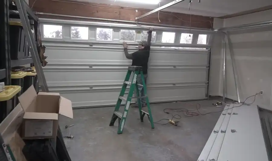 Technician on a ladder repairing a garage door track and spring assembly in a Visalia garage
