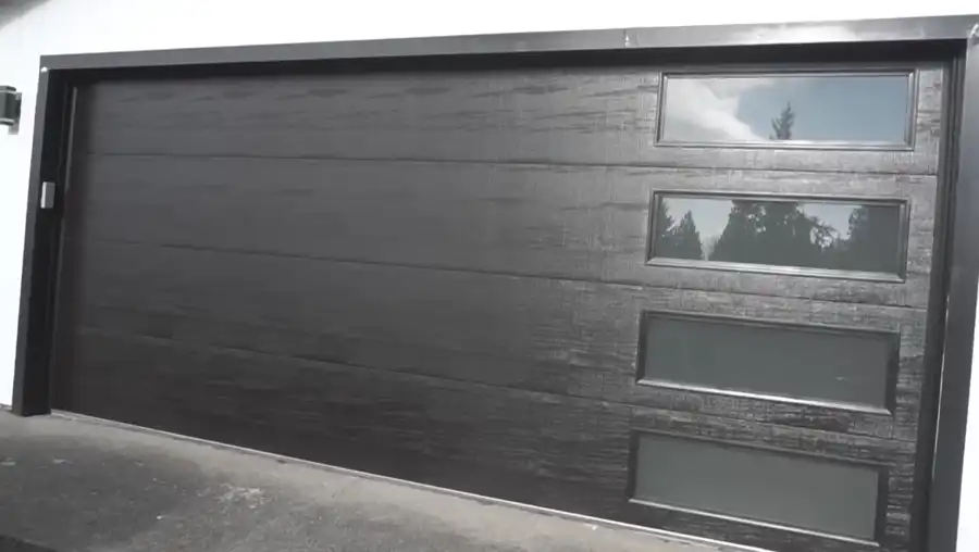 Modern dark wood-grain garage door with glass panel windows installed on a Visalia, CA home