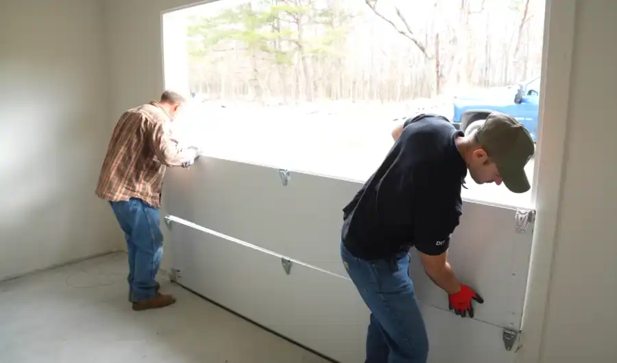 Two technicians lifting a garage door section into place during installation
